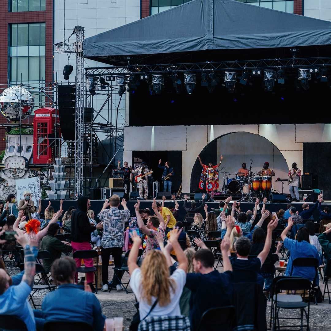 People singing and dancing at the outdoor venue Homeground as a band plays on stage. 