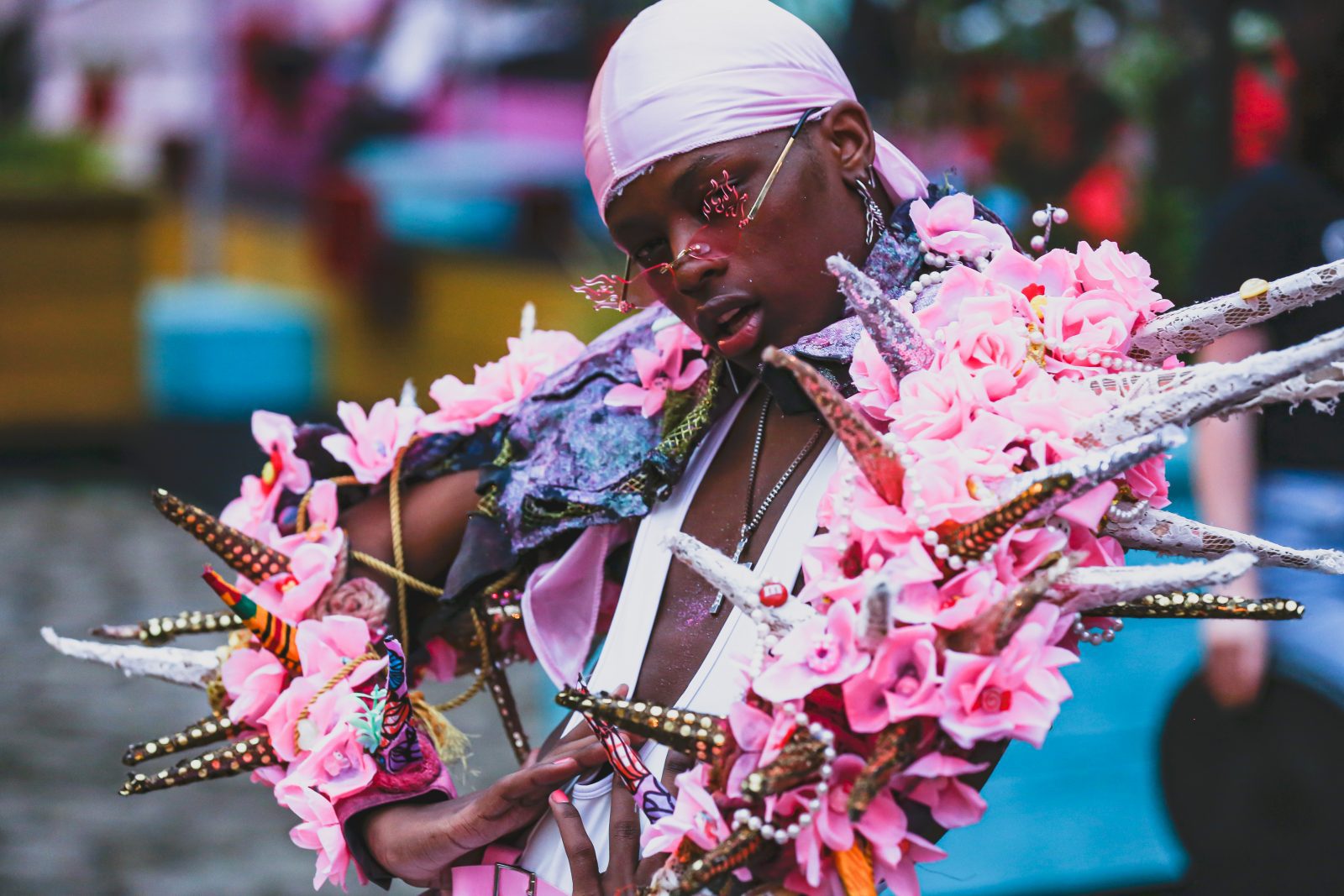 A dancer poses adorned in pink flowers, beads and flame shaped sunglasses. 