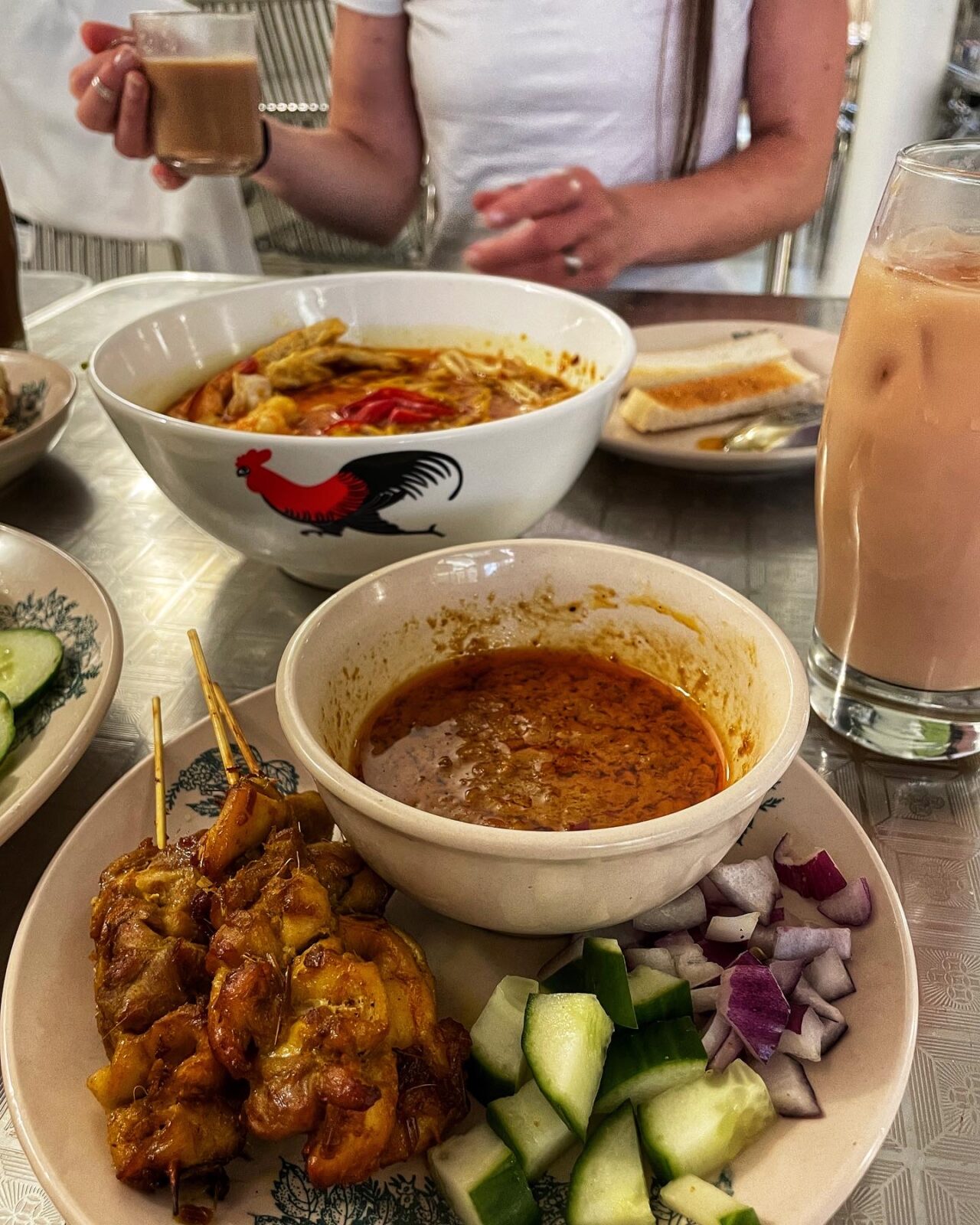 Chicken satay skewers with dipping sauce, cucumber and red onion.